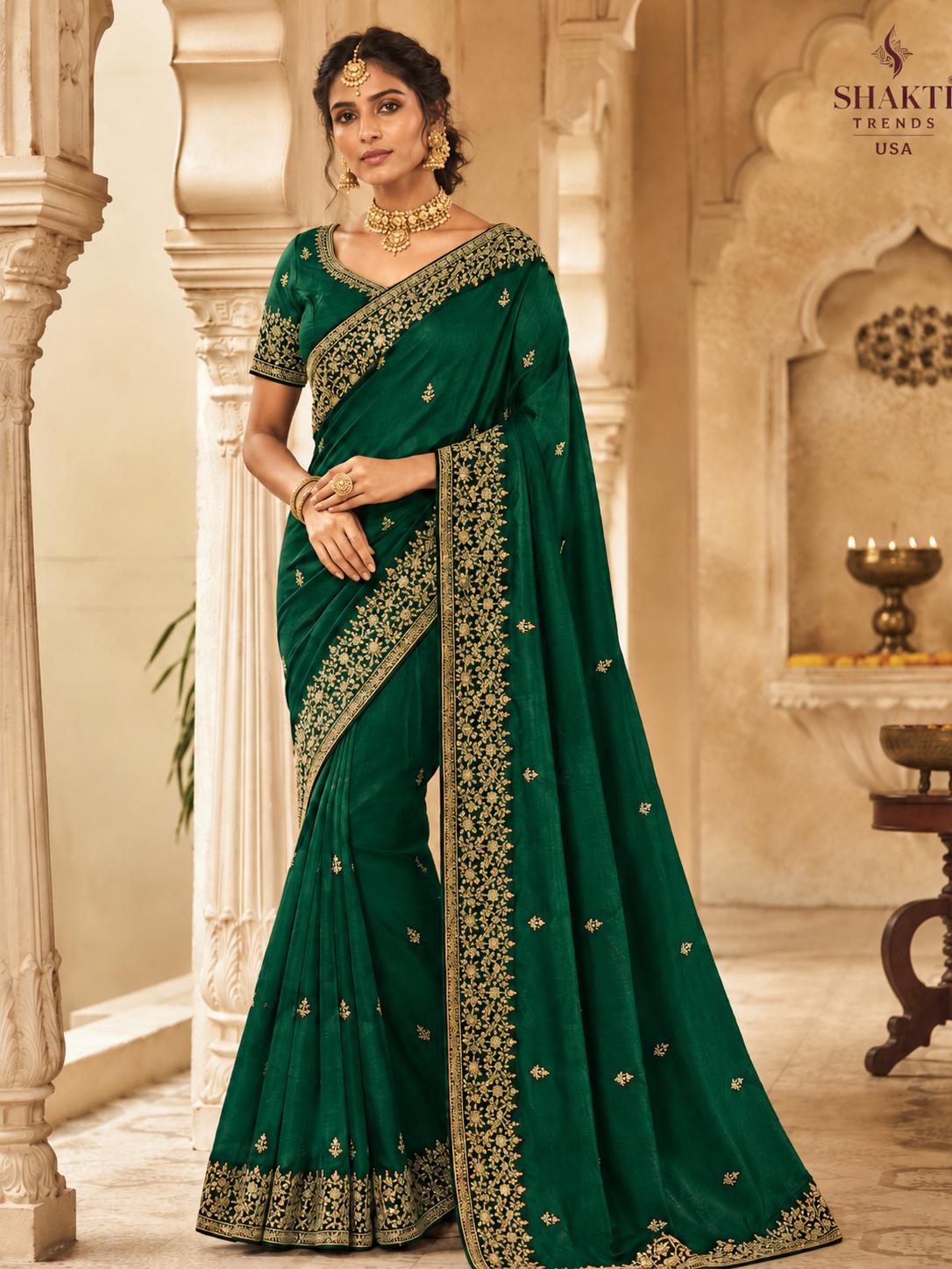 South Asian woman wearing an emerald green traditional saree with gold embroidery and matching jewelry in a palace-style setting.